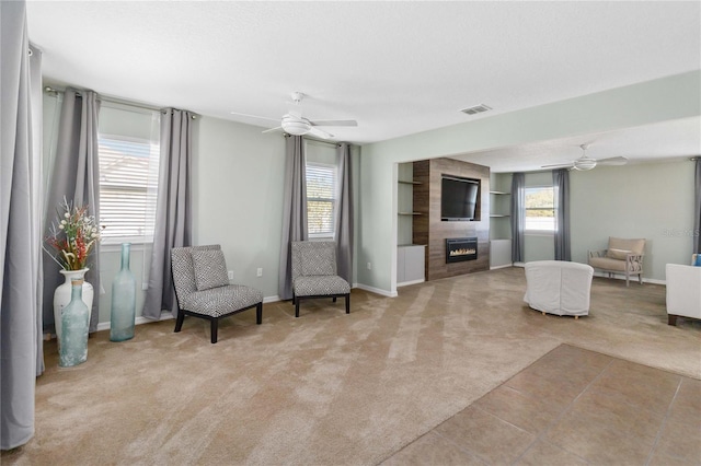 living area with a large fireplace, light carpet, and ceiling fan