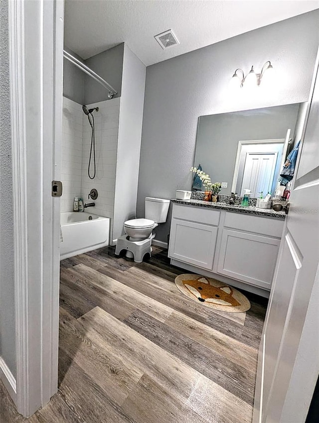 full bathroom with toilet, a textured ceiling, tiled shower / bath combo, hardwood / wood-style flooring, and vanity