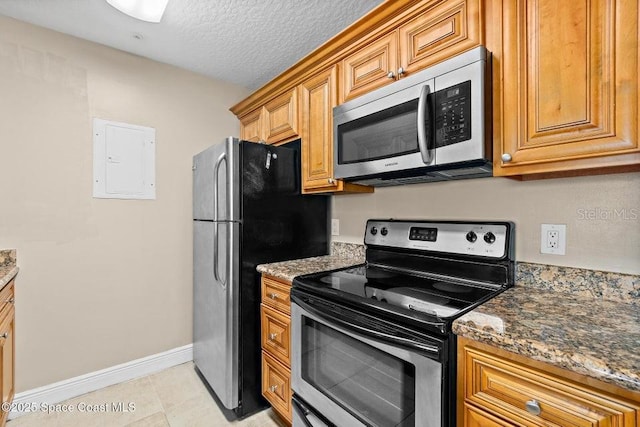 kitchen with light tile patterned floors, a textured ceiling, dark stone counters, and stainless steel appliances