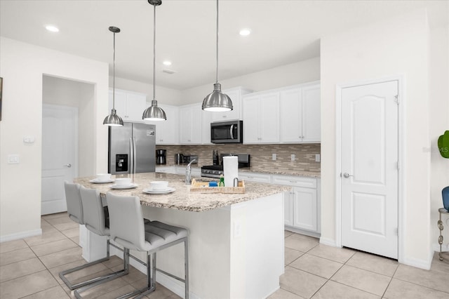 kitchen with white cabinetry, light tile patterned floors, pendant lighting, stainless steel appliances, and a kitchen island with sink