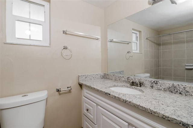 bathroom featuring tiled shower, toilet, and vanity