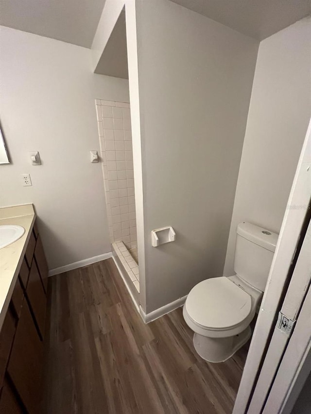 bathroom with hardwood / wood-style floors, toilet, vanity, and a tile shower