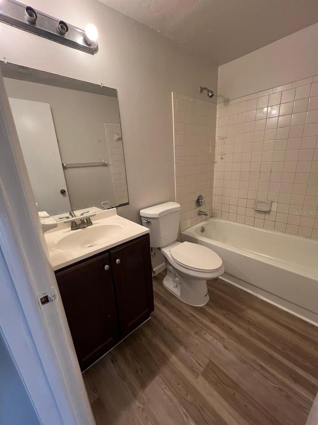 full bathroom featuring wood-type flooring, tiled shower / bath, a textured ceiling, toilet, and vanity