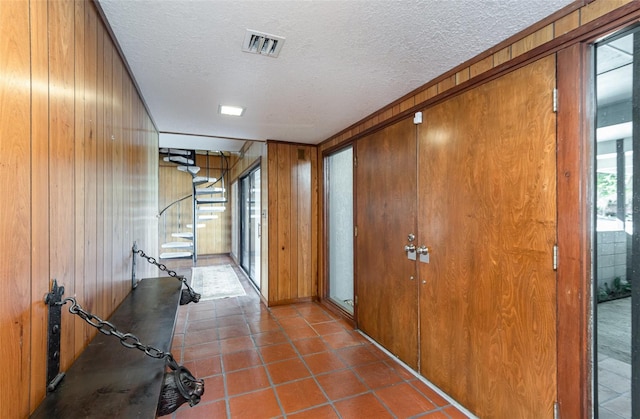 corridor with tile patterned floors, a textured ceiling, and wood walls