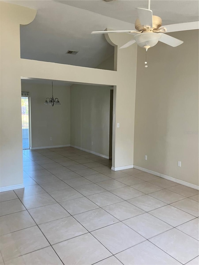 empty room featuring lofted ceiling, light tile patterned floors, and ceiling fan with notable chandelier