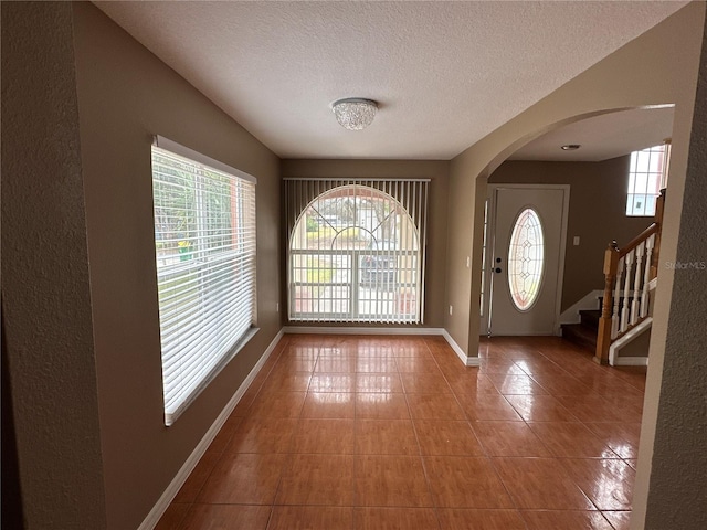 entryway with arched walkways, a textured ceiling, tile patterned flooring, baseboards, and stairs