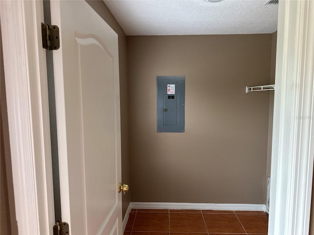 laundry area featuring dark tile patterned flooring, electric panel, a textured ceiling, and baseboards