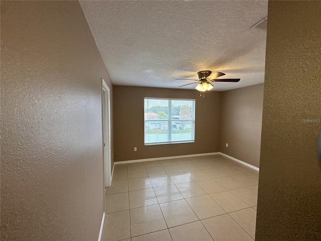 empty room featuring light tile patterned floors, ceiling fan, a textured wall, and baseboards