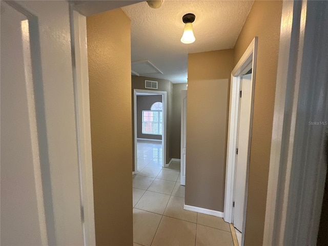 hallway with light tile patterned floors, baseboards, visible vents, and a textured ceiling