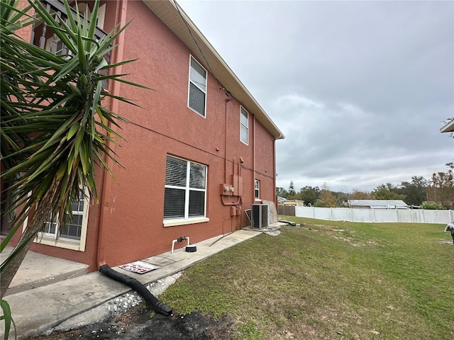 view of property exterior featuring stucco siding, fence, central AC, and a yard