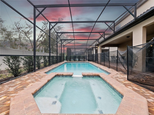 pool at dusk featuring an in ground hot tub and a lanai