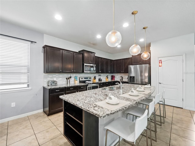 kitchen with dark brown cabinetry, sink, hanging light fixtures, a center island with sink, and stainless steel appliances