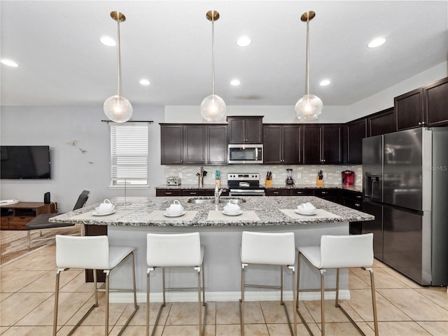 kitchen featuring a kitchen island with sink, hanging light fixtures, light tile patterned floors, and stainless steel appliances