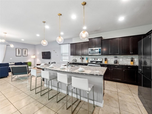 kitchen featuring sink, appliances with stainless steel finishes, a center island with sink, decorative light fixtures, and light tile patterned flooring