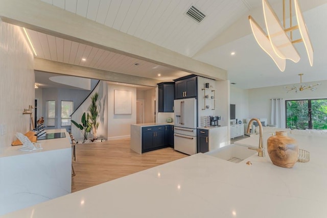 kitchen featuring pendant lighting, sink, high end fridge, light stone counters, and light hardwood / wood-style floors