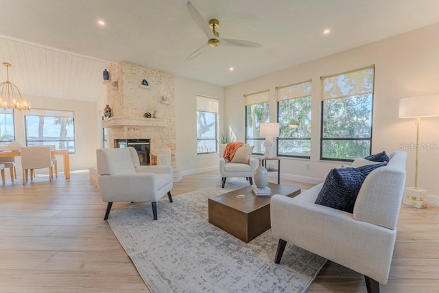 living room featuring a large fireplace, ceiling fan with notable chandelier, and light hardwood / wood-style flooring