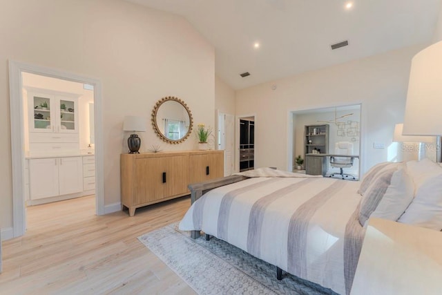 bedroom featuring high vaulted ceiling, ensuite bath, and light hardwood / wood-style flooring