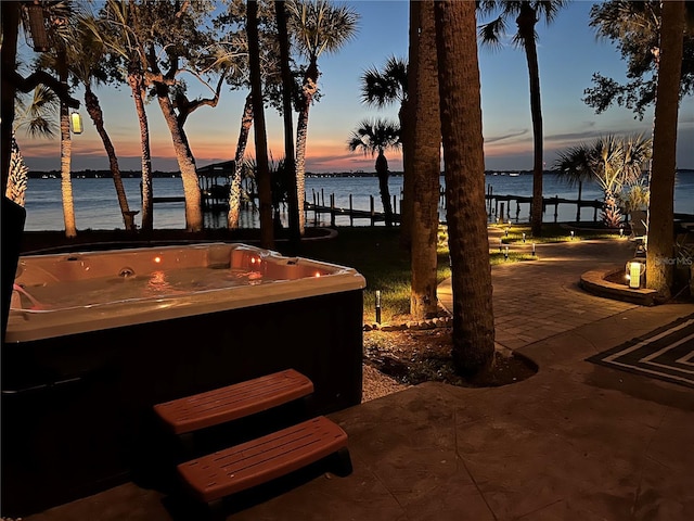 patio terrace at dusk featuring a hot tub and a water view