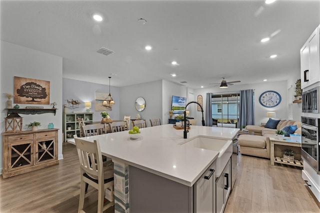 kitchen featuring pendant lighting, appliances with stainless steel finishes, white cabinetry, an island with sink, and a kitchen bar