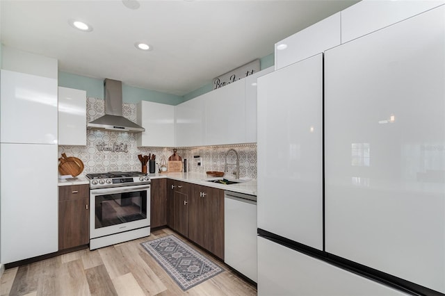 kitchen with wall chimney range hood, sink, stainless steel gas range, dishwasher, and white cabinets