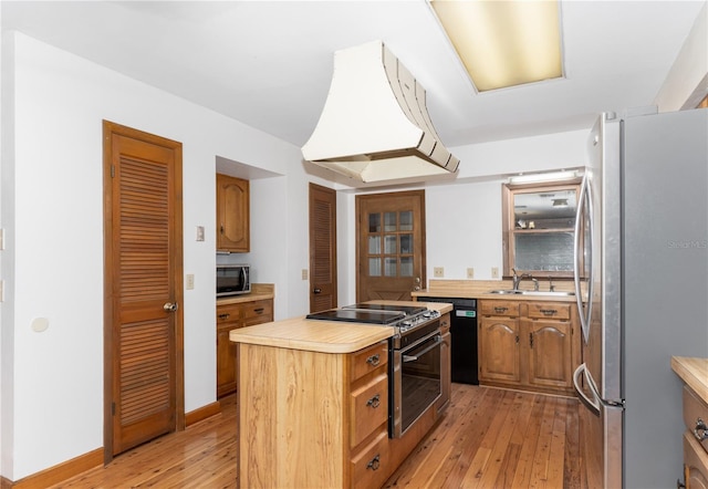 kitchen with sink, premium range hood, appliances with stainless steel finishes, light hardwood / wood-style floors, and a kitchen island