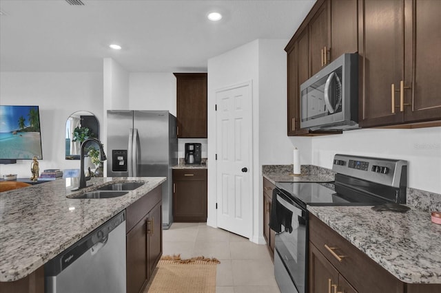 kitchen featuring light tile patterned floors, an island with sink, light stone countertops, stainless steel appliances, and a sink