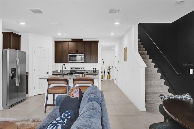 kitchen featuring dark brown cabinetry, visible vents, an island with sink, open floor plan, and stainless steel appliances