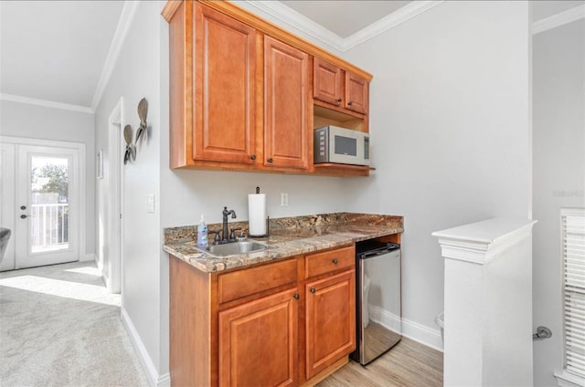 kitchen featuring refrigerator, brown cabinets, crown molding, stainless steel microwave, and a sink