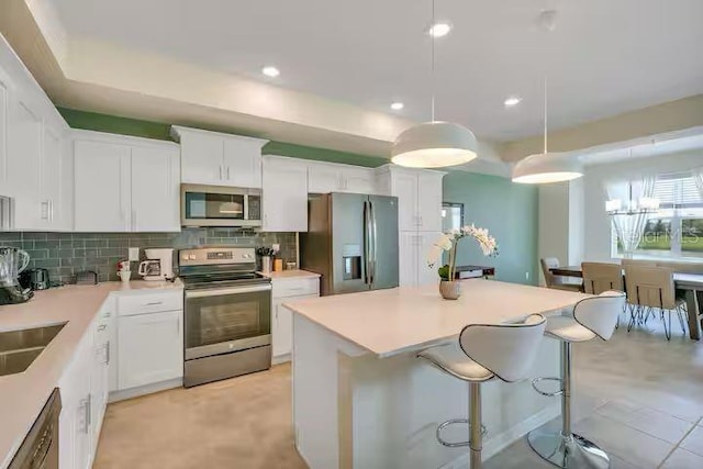 kitchen with white cabinets, stainless steel appliances, pendant lighting, and backsplash