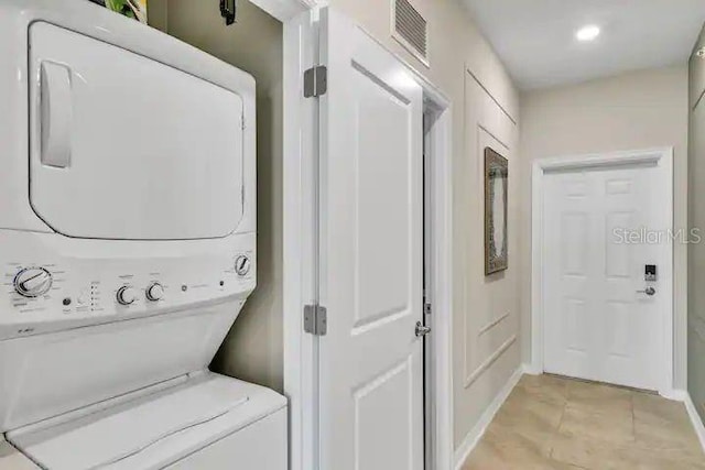 clothes washing area featuring light tile patterned floors and stacked washing maching and dryer