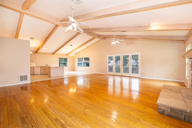 unfurnished living room with beamed ceiling, a wealth of natural light, ceiling fan with notable chandelier, and light hardwood / wood-style flooring