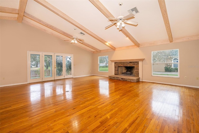 unfurnished living room featuring beamed ceiling, ceiling fan, a stone fireplace, and light wood-type flooring