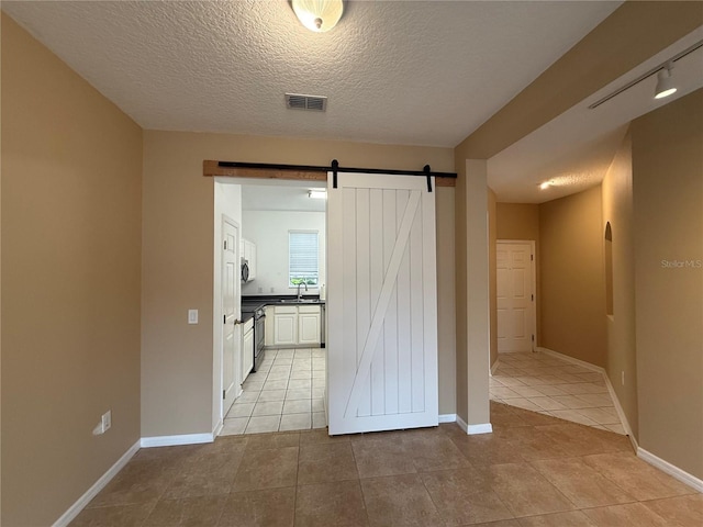 hall with a barn door, sink, a textured ceiling, and light tile patterned floors