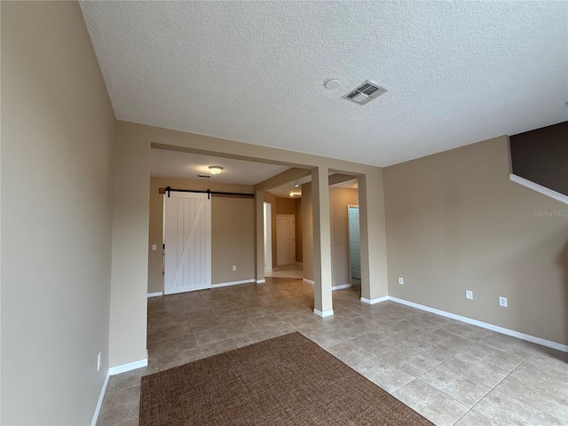 unfurnished room with a barn door, a textured ceiling, and light tile patterned floors