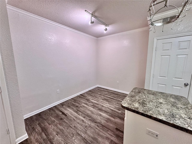 unfurnished dining area with crown molding, dark wood-type flooring, track lighting, and a textured ceiling