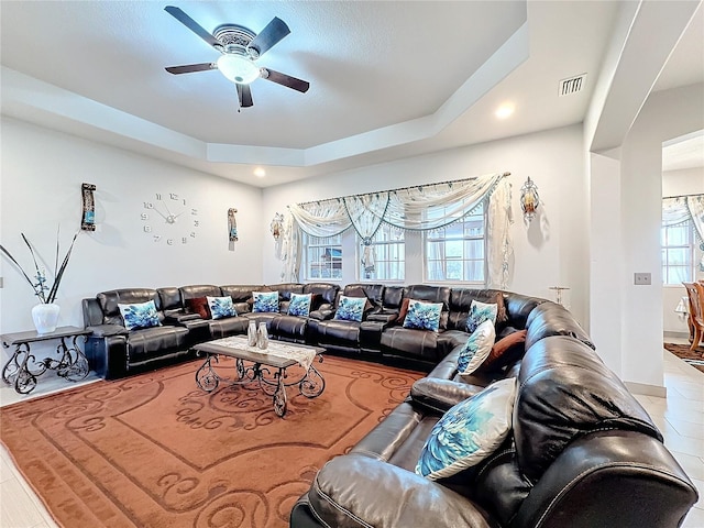 living room with ceiling fan, plenty of natural light, and a raised ceiling