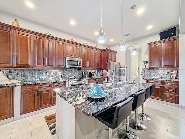 kitchen featuring pendant lighting, a breakfast bar area, dark stone countertops, stainless steel appliances, and a center island with sink