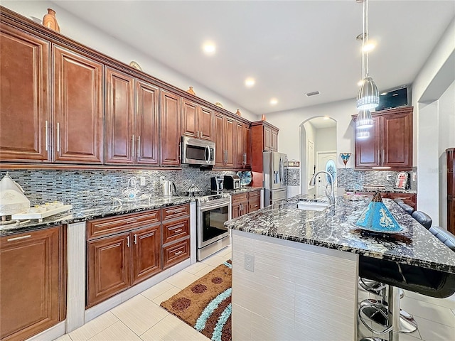 kitchen with a breakfast bar, light tile patterned floors, dark stone countertops, appliances with stainless steel finishes, and pendant lighting