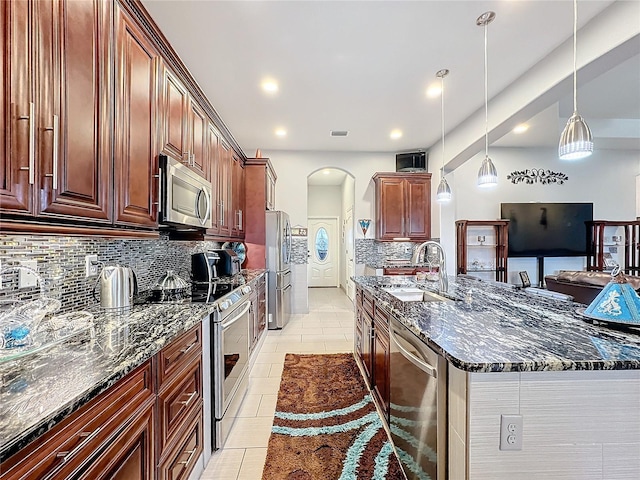 kitchen featuring sink, light tile patterned floors, appliances with stainless steel finishes, dark stone countertops, and decorative light fixtures