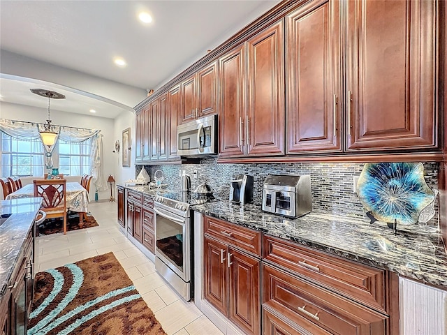 kitchen with light tile patterned floors, dark stone counters, pendant lighting, stainless steel appliances, and decorative backsplash