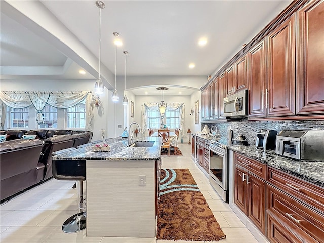 kitchen featuring appliances with stainless steel finishes, a breakfast bar, sink, dark stone counters, and hanging light fixtures