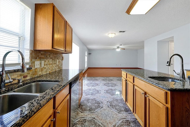 kitchen with stainless steel dishwasher, dark stone counters, and sink