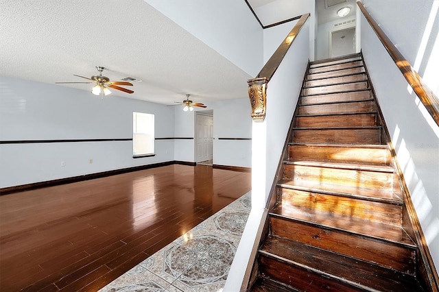 stairway with wood-type flooring, ceiling fan, and a textured ceiling