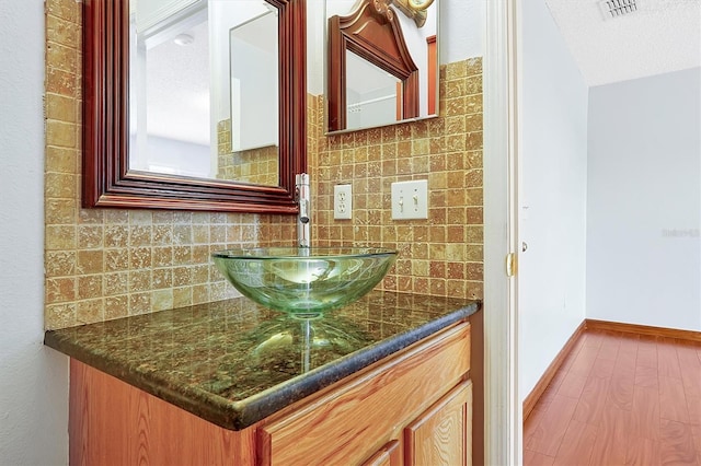 bathroom with vanity, hardwood / wood-style floors, a textured ceiling, and decorative backsplash