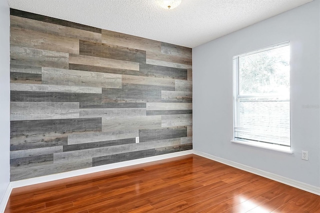 unfurnished room featuring wood-type flooring, a textured ceiling, and wood walls