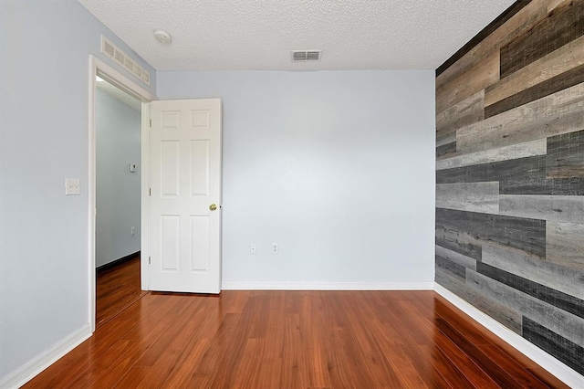 empty room featuring hardwood / wood-style flooring, wooden walls, and a textured ceiling