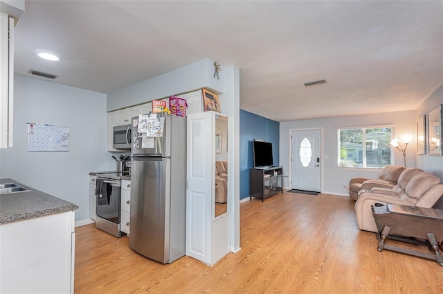 kitchen with appliances with stainless steel finishes, sink, white cabinets, and light wood-type flooring