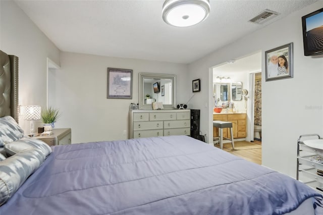 bedroom with a textured ceiling, ensuite bath, and light hardwood / wood-style floors