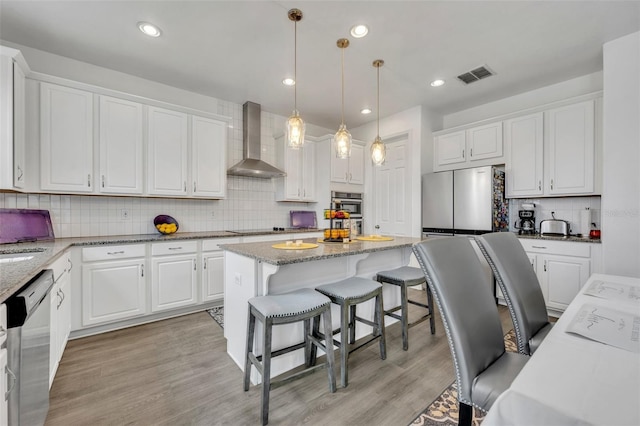 kitchen featuring white cabinetry, appliances with stainless steel finishes, pendant lighting, and wall chimney range hood