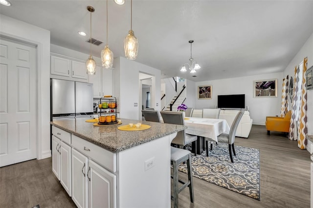 kitchen with a kitchen bar, white cabinetry, light stone counters, decorative light fixtures, and a kitchen island